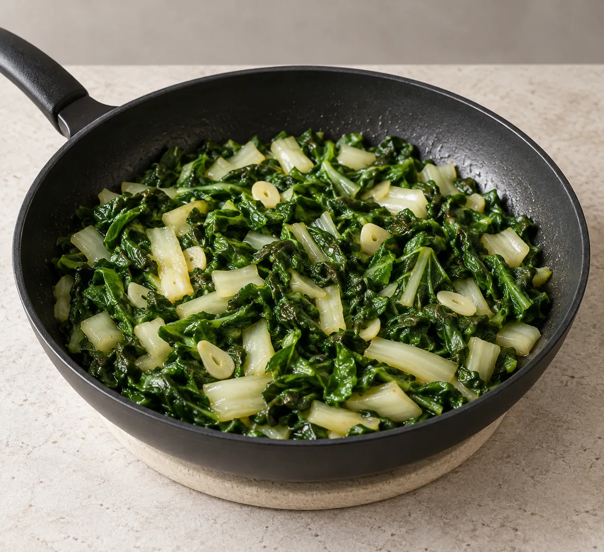 Wilted green Swiss chard, tender white stems and softened garlic slices in a black frying pan.