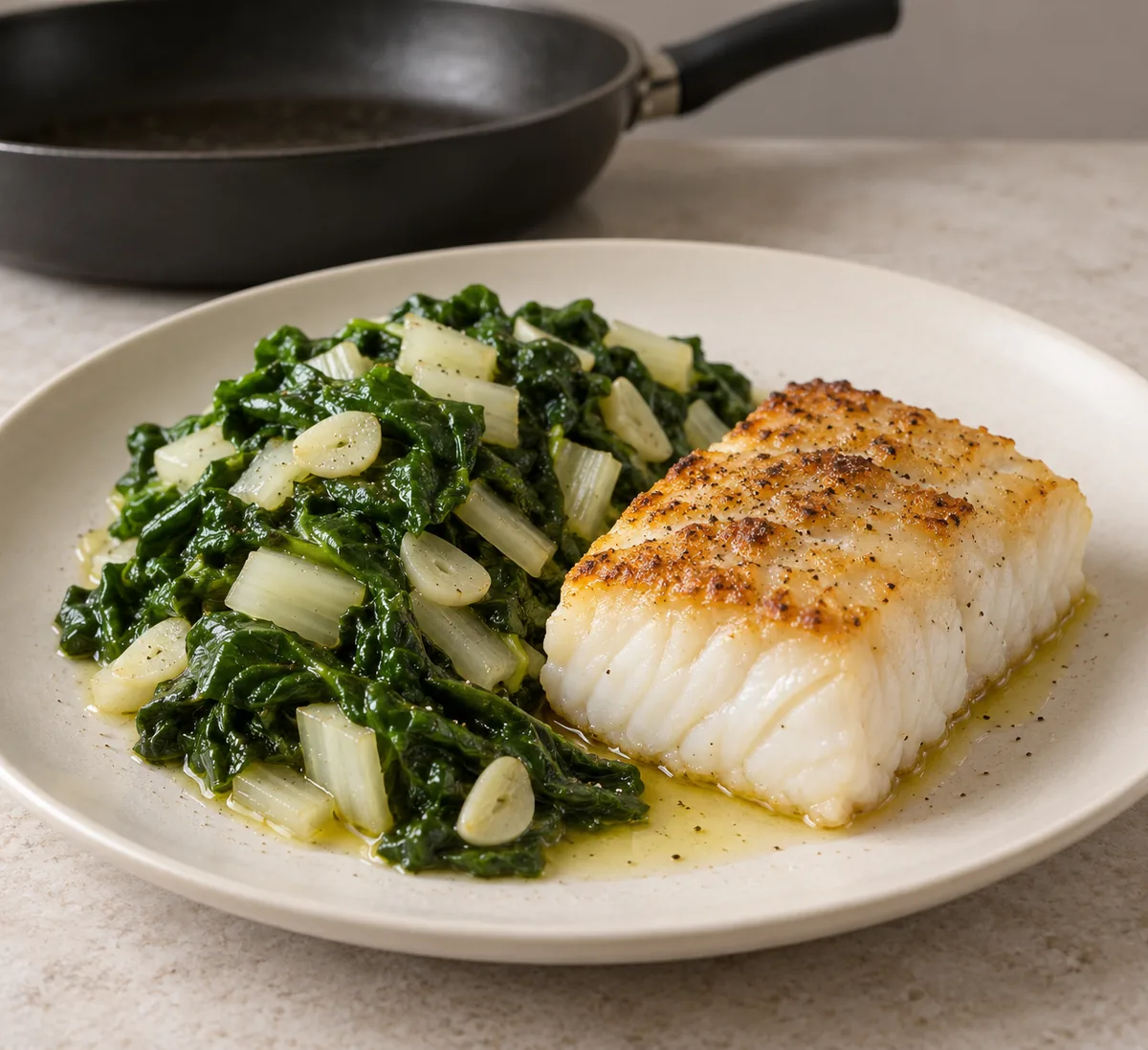 One ivory plate holding golden pan-seared cod and glossy Swiss chard with white stems and sliced garlic.